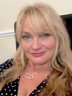 Woman with blonde hair, smiling, wearing a molecular structure necklace and polka dot top.